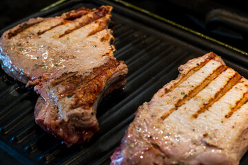 Grilled Pork steaks, neck meat on grill pan. Black background. Top view.