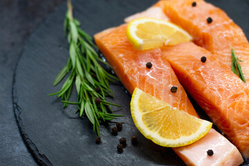 Fresh salmon slices, rosemary, lemon and pepper on dark textured table