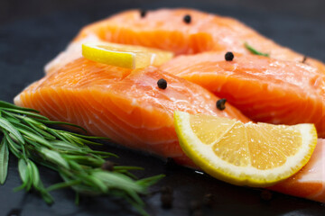 Fresh salmon slices, rosemary, lemon and pepper on dark textured table