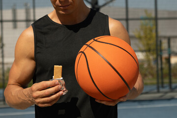 Sports man or basketball player eating energy bar. Muscular athlete snacks on protein bar while...