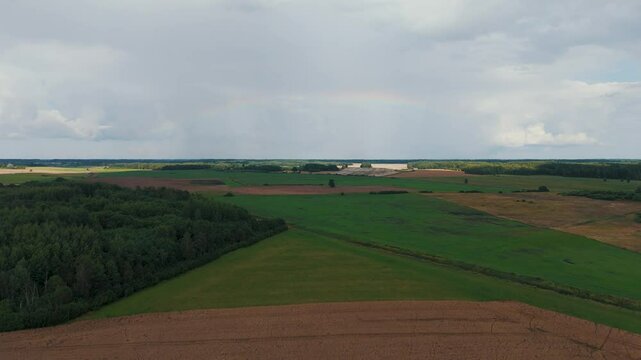 The Rainbow Over the Green Field After Storm With Rain, During Outumn, Aerial View Under Heavy Clouds Before Thunderstorm. Agriculture Landscape Many Crop Fields. Aerial 4k Shot