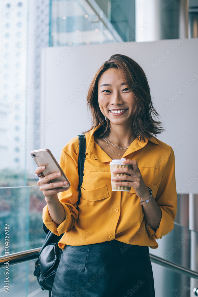 Poster half length portrait of cheerful hipster girl with smartphone mobile gadget in hand looking at camer