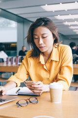 Attractive Asian woman student checking received email on cellphone gadget during e learning in university space, Japanese skilled female freelancer updating notification on smartphone device