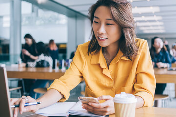 Attractive Chinese student sharing media files for presentation between laptop and cellphone device...