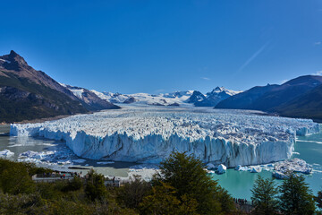 Obraz premium Majestic Perito Moreno Glacier in Argentina’s Los Glaciares National Park, with jagged ice peaks, turquoise waters, and rugged mountains under a clear blue sky
