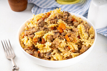 Easy homemade pasta with minced meat. One pot pasta with ground beef and autumn vegetables, in portioned plate on kitchen table