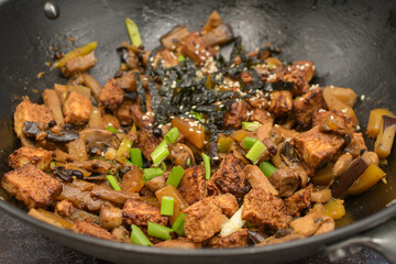 Crispy tofu stir fried in wok along with  mushrooms and  eggplant