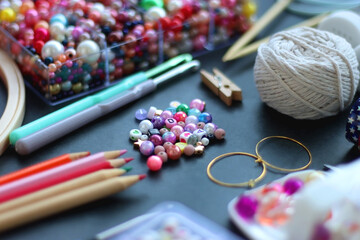 Colorful beads, coloring pencils, glitter, needles, string, hoop, tape and scissors on dark...