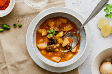 Gulaschsuppe mit Rindfleisch und Kartoffeln in einem Teller auf einem grauen Tisch. Draufsicht, Abendessen, servierfertig.
