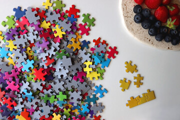 Colorful jigsaw puzzle pieces, cup of tea or coffee, eyeglasses and fresh berries for snacking. Hygge at home. Top view.