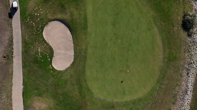 Aerial view of a golf course with sand traps and a golf cart on the path during a sunny afternoon