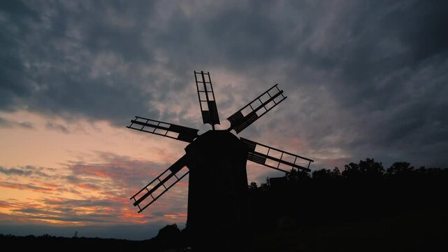 Silhouette of an old windmill at sunset with vibrant clouds in the sky.