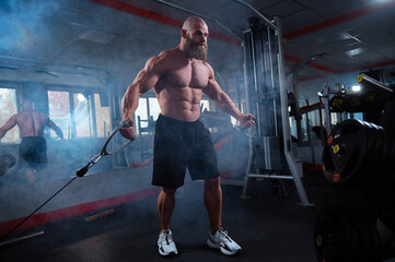 Bald Caucasian bodybuilder training chest using cable crossover in gym. 