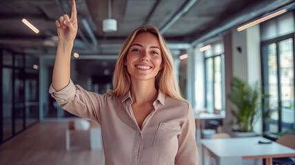 Fototapeta premium Smiling blonde woman in a casual shirt pointing upwards to the right with a confident stance, modern office environment. Ai generated