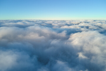 Aerial view from above at high altitude of dense puffy cumulus clouds flying in evening. Amazing sunset from airplane window point of view