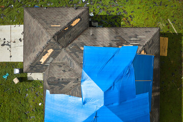 Aerial view of damaged in hurricane Ian house roof covered with blue protective tarp against rain...