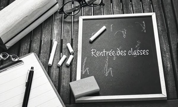 Rentr&eacute;e des classes en noir et blanc, avec une ardoise marqu&eacute;e en fran&ccedil;ais "Rentr&eacute;e des classes" &agrave; la craie, entour&eacute;e de stylos, craies, &eacute;ponges, trousse en bois, bloc-notes et lunettes de vue