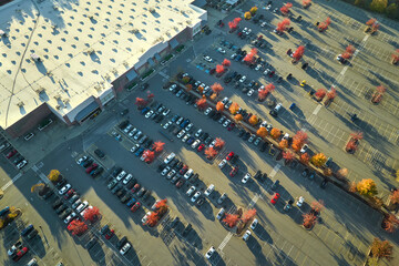 Aerial view of large parking lot in front of rgocery store with many parked colorful cars. Carpark at supercenter shopping mall with lines and markings for vehicle places and directions