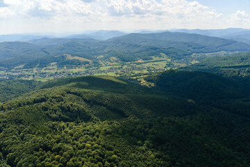 Fototapeta premium Aerial view of mountain hills covered with dense green lush woods on bright summer day