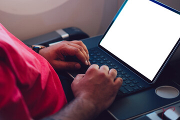 Young man flight passenger connecting to wireless internet on board with touch pad while sitting next to aircraft cabin window. Mock up blank screen for web template, digital nomad work on freelance
