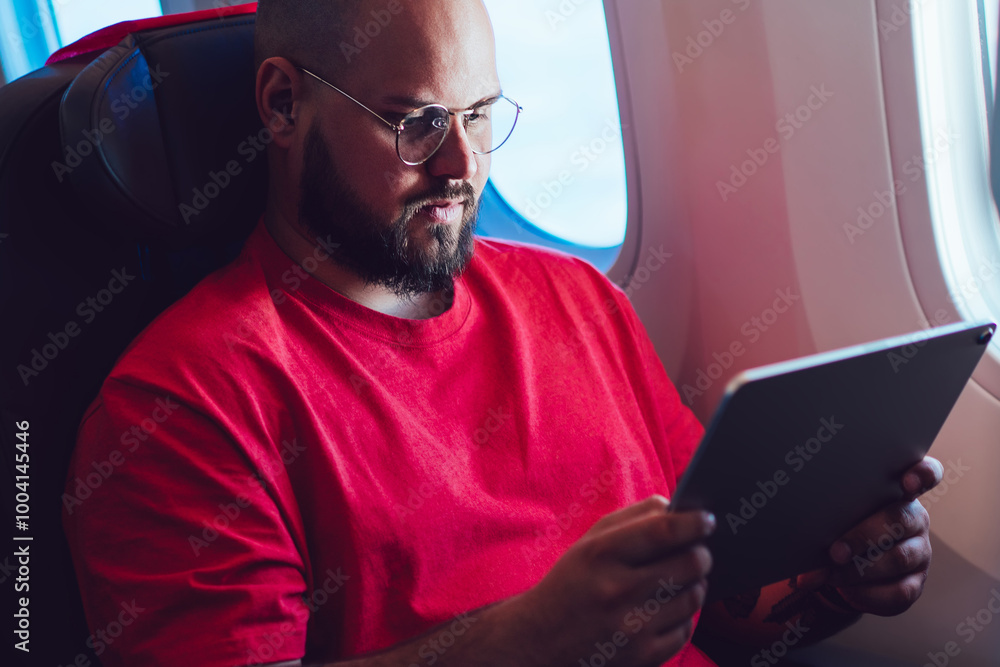 Poster caucasian man aircraft passenger sitting with tablet hands next to airplane window in business class