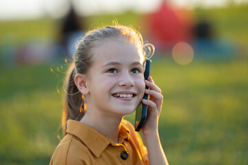 Child girl talking with her friend on cellphone outdoors in summer park