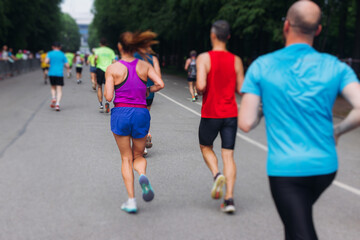 Marathon runners crowd, sportsmen participants start running the half-marathon in the city streets, crowd of sportswomen joggers in motion, group athletes outdoor training competition in a summer day