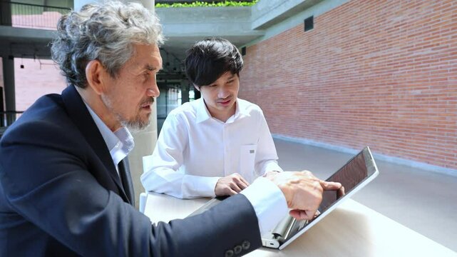 Asian senior professor is giving advice to the college student on the research thesis while sitting in the university faculty for education, academic and business