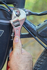 one industrial adjustable shiny iron new small chrome mechanical wrench in hand unscrews working nut on black frame of sport mountain bike daytime outdoors