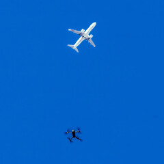 A commercial airplane flying high above while a drone operates below on a clear blue sky day