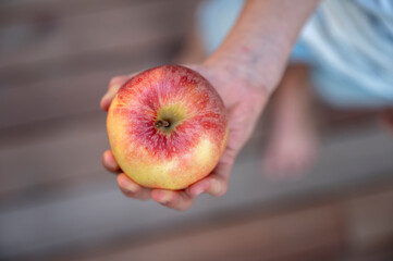 Top view of a child holding a juicy ripe apple in his hand