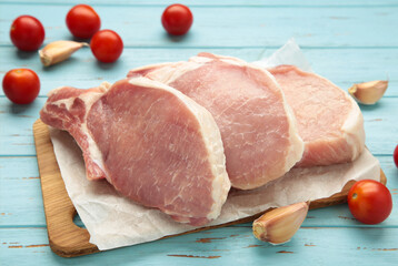 Sliced raw pork meat on cutting board on blue wooden background.