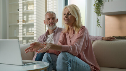 Fototapeta premium Happy satisfied Caucasian married couple grandfather grandmother man woman talking on video call using laptop at home couch online meeting with relatives communicate via computer webcam family support