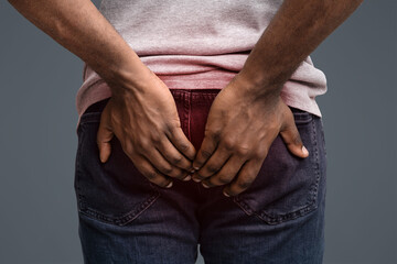 Afro man with hemorrhoids holding his butt in pain, white background, cropped