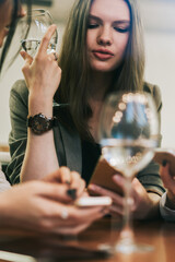 Attractive caucasian women installing application for communicate online via cellular phones during free time for drinking wine togetherness and socialising, concept of technology and generation