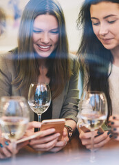 Happy smiling female friends enjoying from spending time togetherness in cafe interior during holidays watching funny videos online on comedy content websites via new modern smartphone gadgets