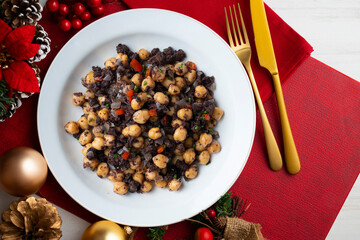 Sautéed chickpeas with black pudding and vegetables. Top view table with Christmas decoration.