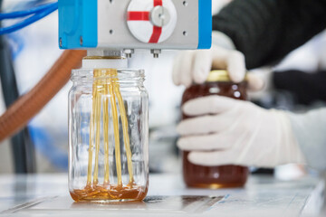 Filling empty jars with fresh honey in factory.