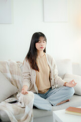 An Asian woman meditating on a sofa.
