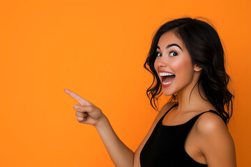 Beautiful girl posing on orange background and pointing finger at place for advertisement and text