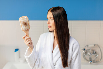 Hair loss problem. Sad lady looking at comb full of fallen hair, suffering alopecia or lack of...
