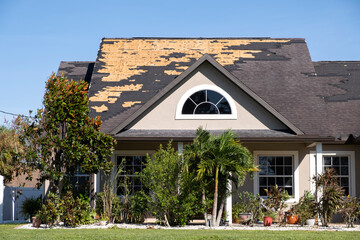 Wind damaged house roof with missing asphalt shingles after hurricane Ian in Florida. Repair of...