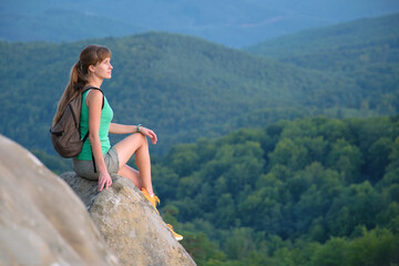 Naklejka premium Woman hiker seated alone on rocky mountain cliff enjoying view of evening nature on wilderness trail. Active way of life concept