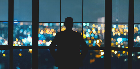 Business Success. Businessman's Silhouette Looking Through Panoramic Window At Night City View Standing Back To Camera In Modern Office. Panorama © Prostock-studio