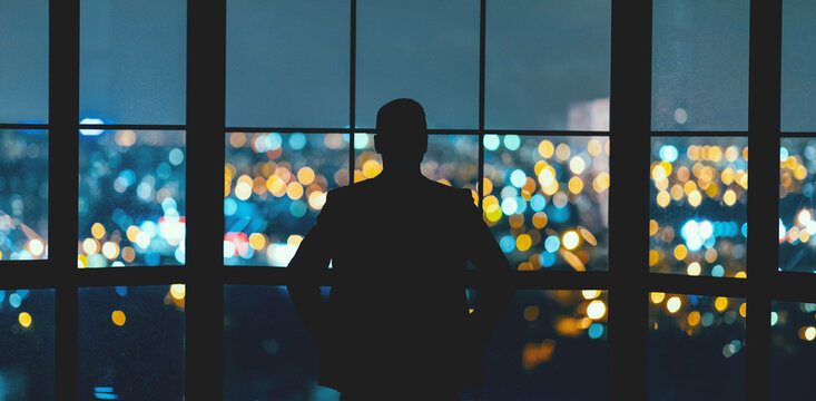 Business Success. Businessman's Silhouette Looking Through Panoramic Window At Night City View Standing Back To Camera In Modern Office. Panorama