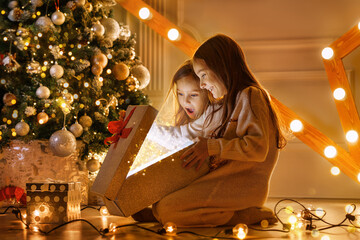 Happy sibling girls opening christmas presents. Children with gift boxes and christmas star. Decorated living room with traditional fire place.