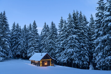 Fairy Christmas landscape with glowing wooden cabin in snowy forest. Cozy house in winter mountains