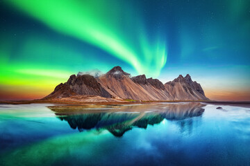 Aurora borealis Northern lights over famous Stokksnes mountains on Vestrahorn cape. Reflection in the clear water on the epic skies background, Iceland. Landscape photography