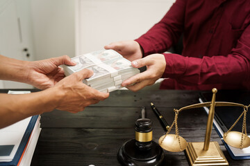 A male lawyer works at his desk, receiving cash from a client while considering the case. He focuses on law, justice, fairness, and the observance of legal rules and conventions in the system