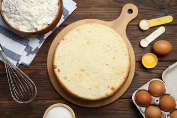 Delicious cut sponge cake, whisk and ingredients on wooden table, flat lay